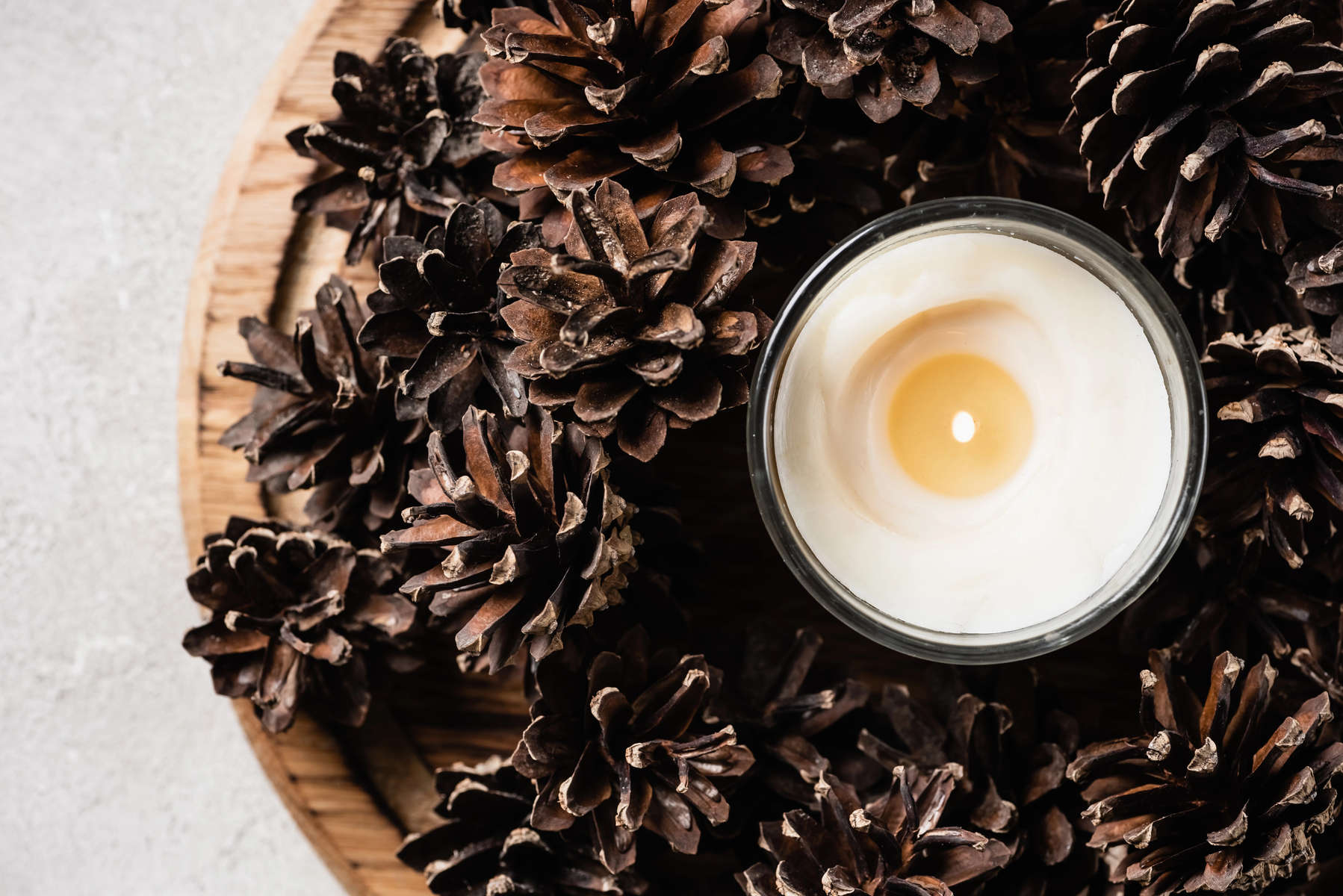 Top view of scented candle with pine cones on wooden plate 